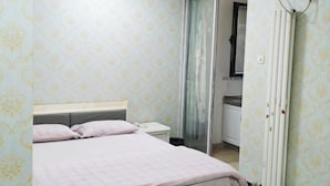 A bedroom with a bed, nightstand, and a bathroom visible through a glass door. - Shanghaojia Apartment (Zhengzhou Digital Harbor) (Zhengzhou)