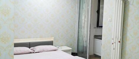 Un dormitorio con cama, mesita de noche y baño visible a través de una puerta de cristal.