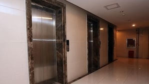 A hallway with two elevators, a polished floor, and a door with a framed picture. - Shanghaojia Apartment (Zhengzhou Digital Harbor) (Zhengzhou)