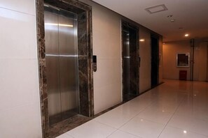 A hallway with two elevators, a polished floor, and a door with a framed picture. - Shanghaojia Apartment (Zhengzhou Digital Harbor) (Zhengzhou)
