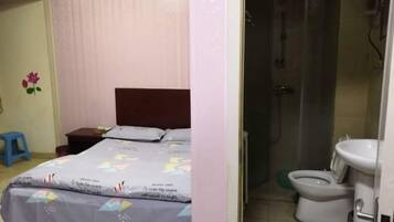 A bedroom with a bed, a nightstand, and a small stool. There is a bathroom with a toilet, sink, and shower.