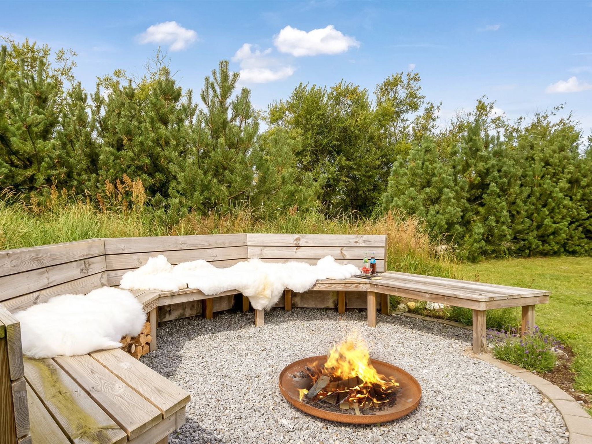 A wooden bench with a fire pit in the center, surrounded by a gravel area.