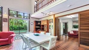 A spacious room with a large dining table, a red sofa, and a view of the outdoors. - Tropical Crush | 4 Beds, 2 Bath | Pool (Fannie Bay)
