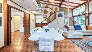 A spacious dining area with a long table, white chairs, and a staircase leading to an upper level. - Tropical Crush | 4 Beds, 2 Bath | Pool (Fannie Bay)