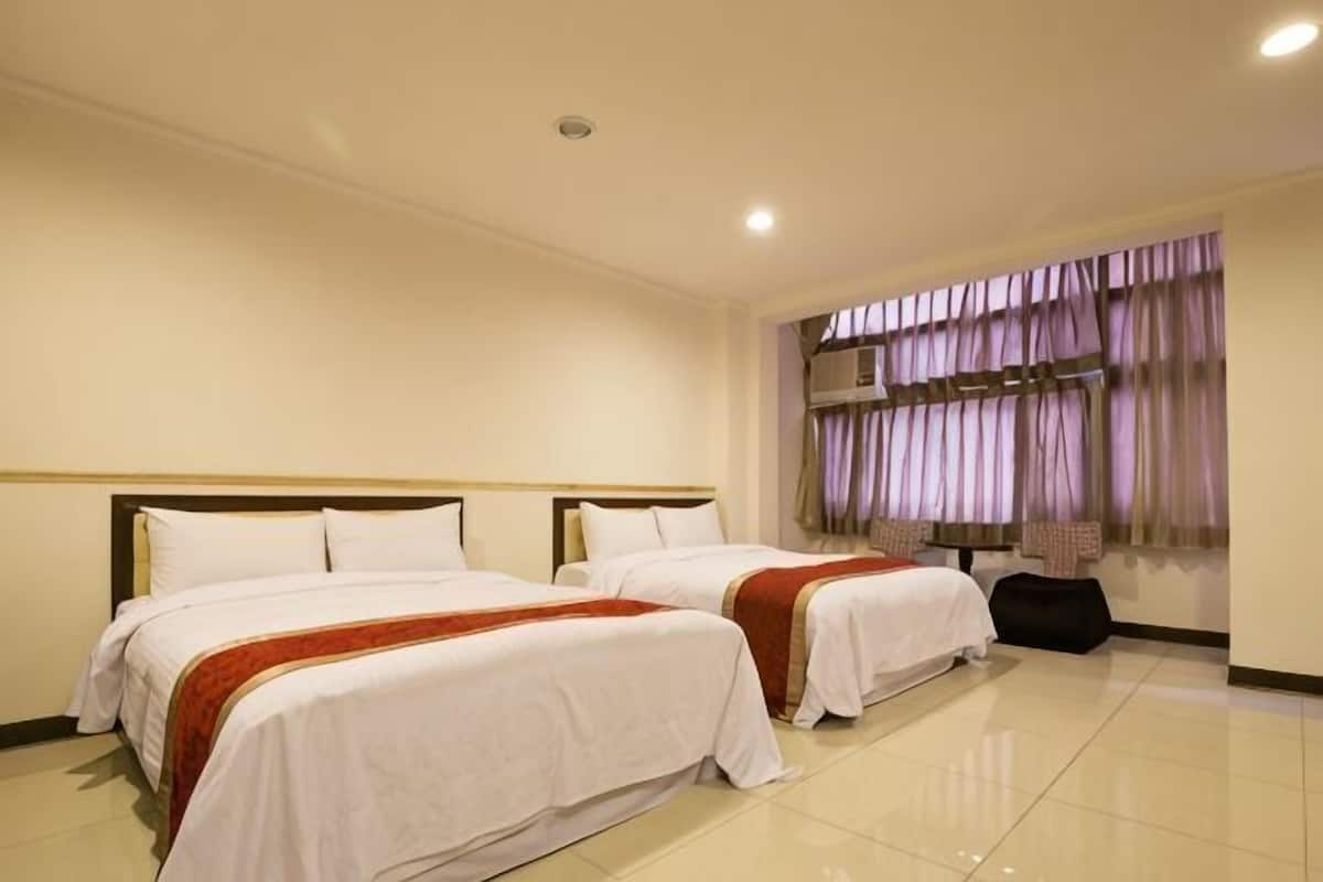 A hotel room with two beds, a large window with curtains, and a suitcase on the floor.