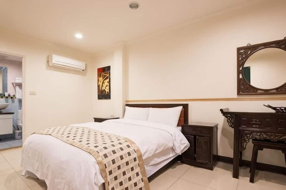 A hotel room with a bed, bedside table, dresser, and a mirror on the wall.