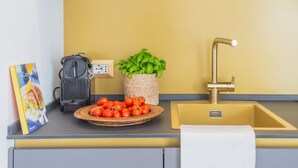 A kitchen counter with a basket of tomatoes, a coffee maker, a plant, and a sink with a gold faucet. - Como Dreams Apartments (Como)