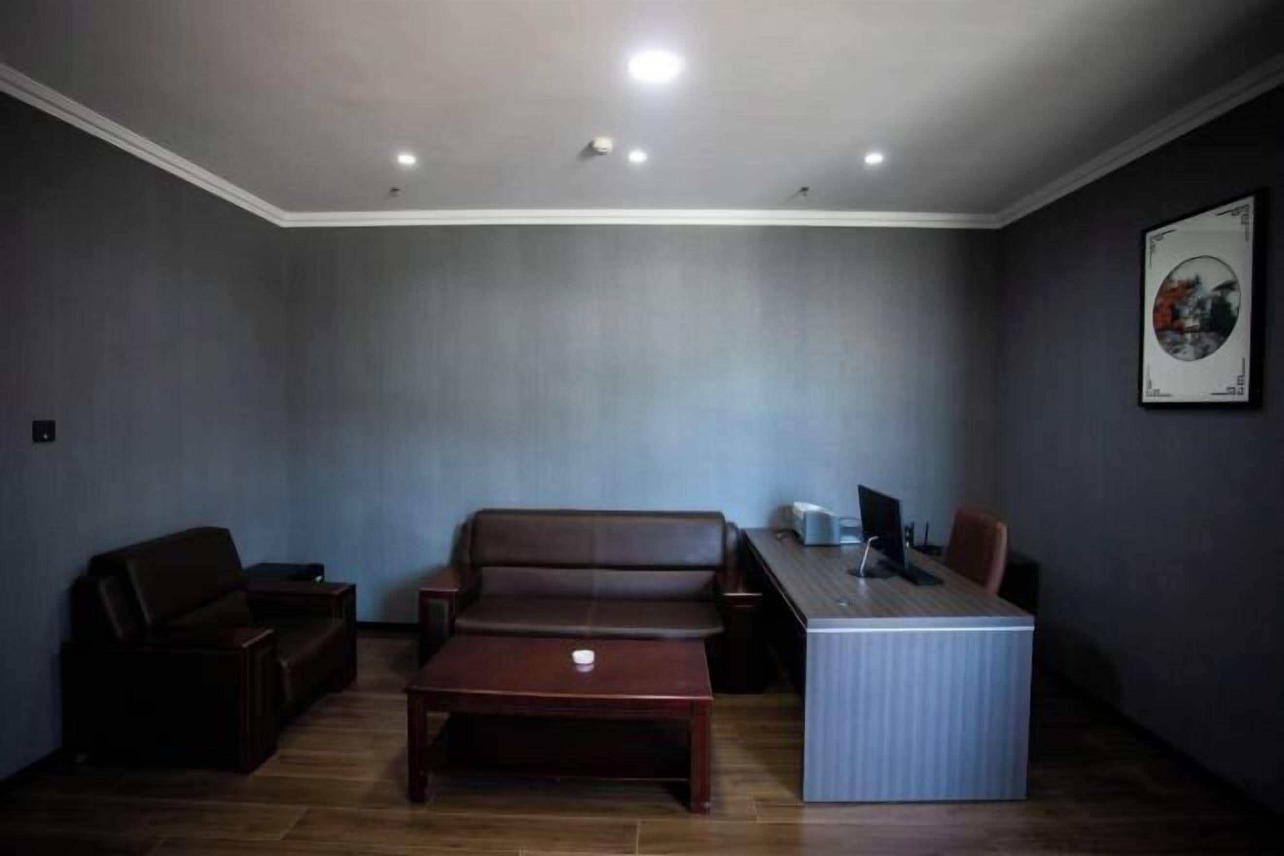A room with a brown leather sofa, a wooden coffee table, a desk with a computer, and a framed picture on the wall.