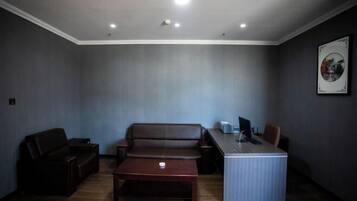 A room with a brown leather sofa, a wooden coffee table, a desk with a computer, and a framed picture on the wall.