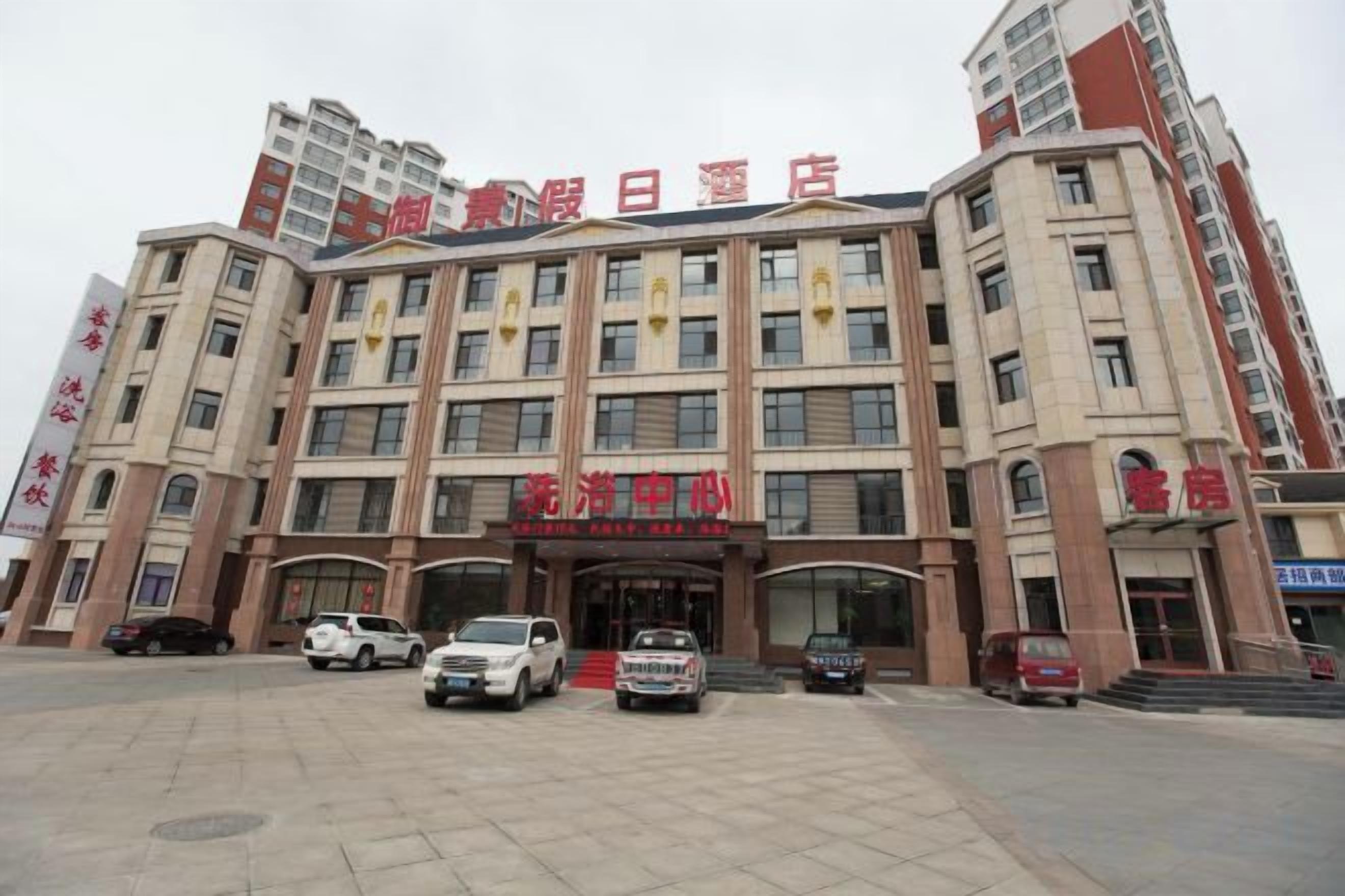 A multi-story hotel with a central entrance, several vehicles parked in front, and a large parking area.