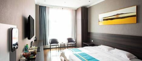 A hotel room with a bed, a desk with a chair, a TV, and a window with curtains.