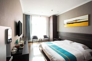 Ett hotellrum med en säng, ett skrivbord med en stol, en TV och ett fönster med gardiner.