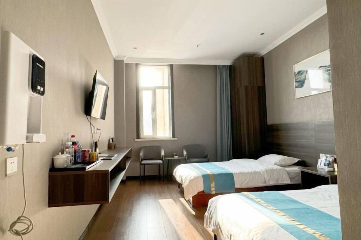 Habitación de hotel con dos camas, un escritorio, una silla, un televisor y una ventana con cortinas.