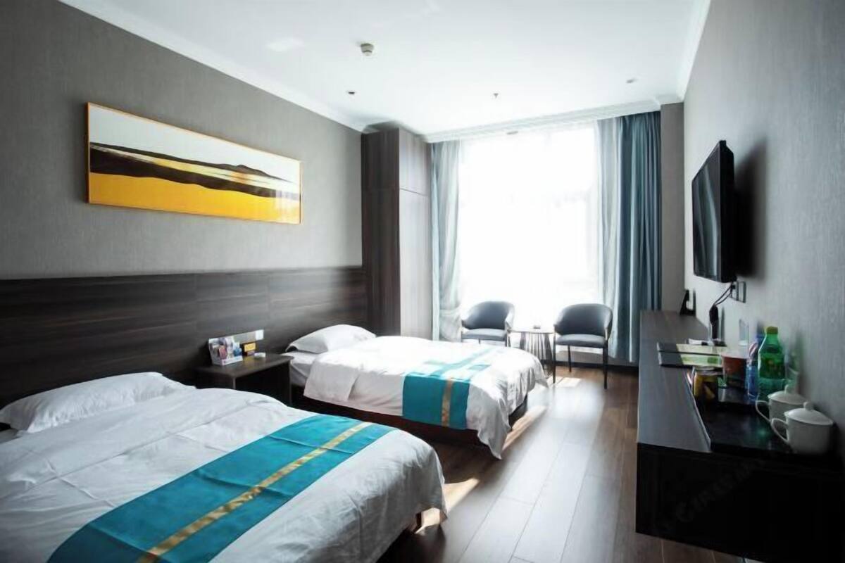 Habitación de hotel con dos camas, televisión, escritorio y un amplio ventanal.