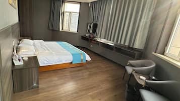 A modern hotel room with a bed, bedside table, TV, and seating area.