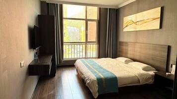 A hotel room with a bed, a TV, a window with curtains, and a painting on the wall.