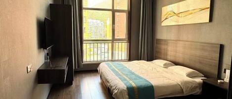 A hotel room with a bed, a TV, a window with curtains, and a painting on the wall.