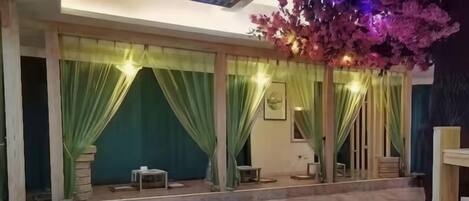 A spacious indoor area with a tiled floor, green curtains, and a seating arrangement.
