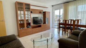 Ein modernes Wohnzimmer mit einem Glastisch, einer Holz-Unterhaltungseinheit und einem Balkon mit Essbereich.
