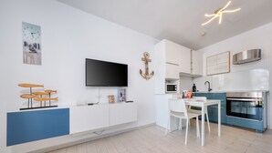 A modern kitchen with a flat-screen TV, a dining area with a white table and chairs, and a blue accent wall. - Vela Azul  • A/C, Pool & Tennis (Puerto del Carmen)