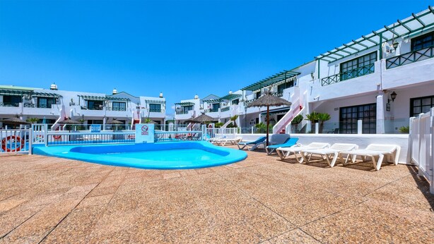 A rooftop pool area with lounge chairs, a blue pool, and white buildings with balconies. - Vela Azul  • A/C, Pool & Tennis (Puerto del Carmen)