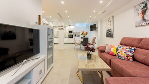 A modern living room with a flat-screen TV, a glass coffee table, and a red sofa with colorful cushions. - Corazón de Triana. Terrace & private pool (Sevilla)