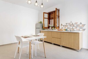 Une cuisine moderne avec une table à manger blanche, des chaises blanches, des meubles de rangement en bois et des œuvres d’art géométriques accrochées au mur.
