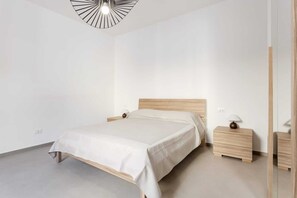 Une chambre à coucher au style minimaliste, avec un lit, des tables de chevet et un luminaire moderne.