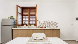 Een moderne keuken met een eettafel gedekt voor twee personen, een koelkast, houten keukenkastjes en een raam met houten luiken.