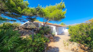 A white building with a tiled roof, surrounded by lush greenery and a clear blue sky. - Villa Bel in La Maddalena (La Maddalena)