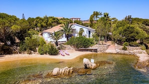 A coastal property with a clear pool, a white house with a red roof, and surrounding greenery. - Villa Bel in La Maddalena (La Maddalena)