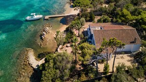 An aerial view of a coastal property with a boat docked near the beach, a house with a tiled roof, and surrounding vegetation. - Villa Bel in La Maddalena (La Maddalena)