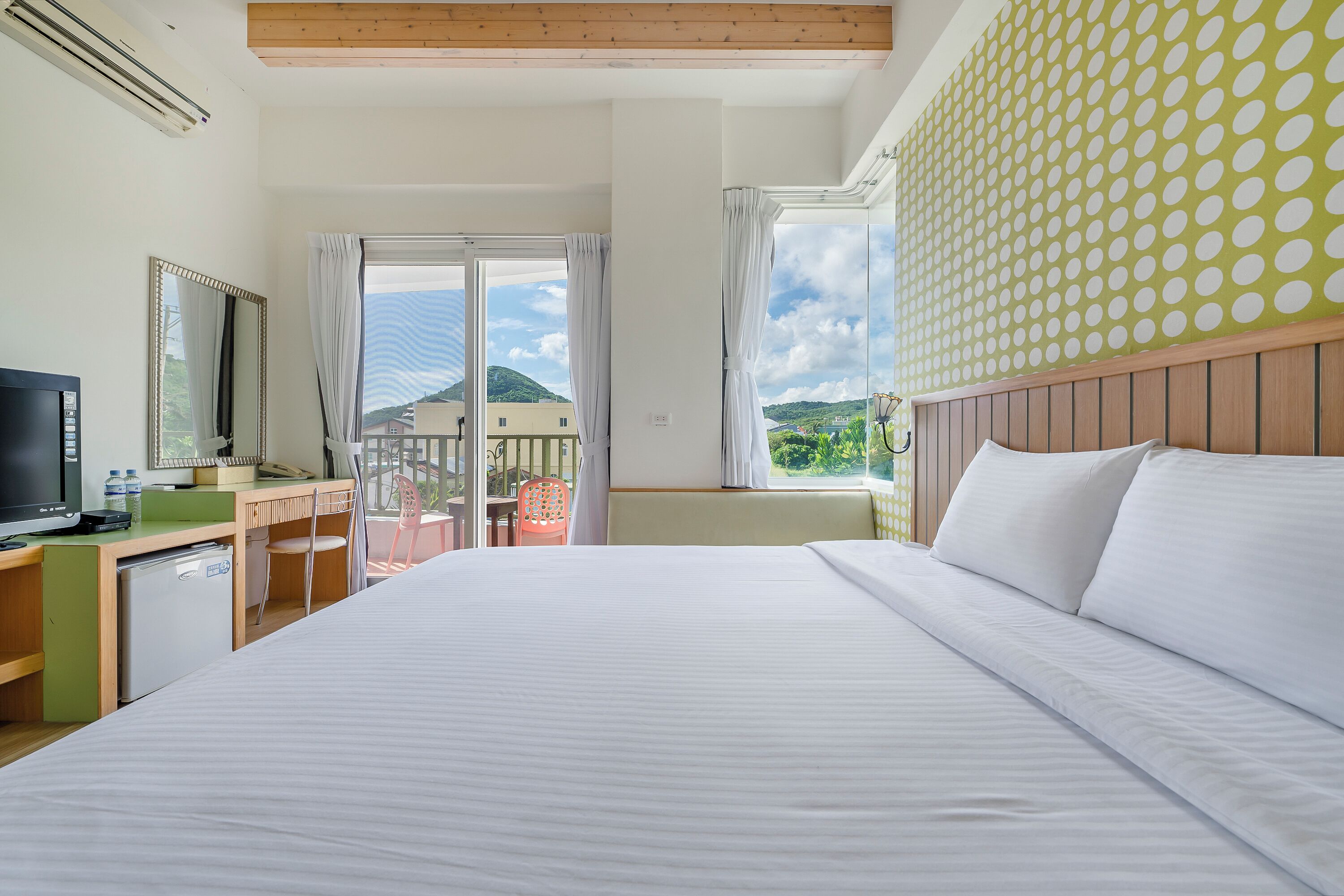 A hotel room with a large bed, a desk with a computer, a TV, and a view of the outdoors.