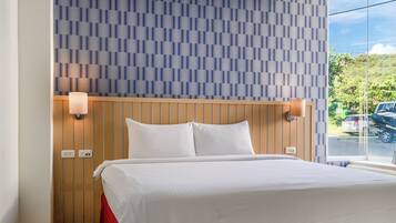 A hotel room with a bed, wooden headboard, two wall-mounted lamps, and a window with a view of a parking area.