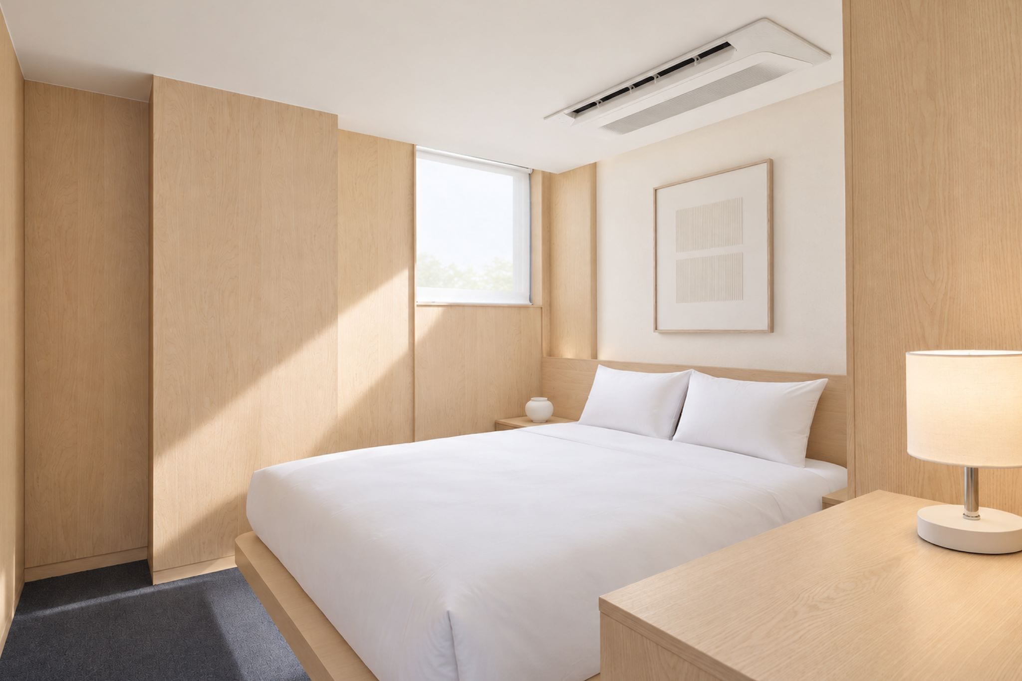 A modern hotel room with a large bed, a bedside table, a lamp, a window, and an air conditioning unit.
