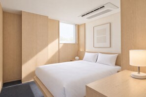 A modern hotel room with a large bed, a bedside table, a lamp, a window, and an air conditioning unit. - UH Suite The Gangnam (Seoul)