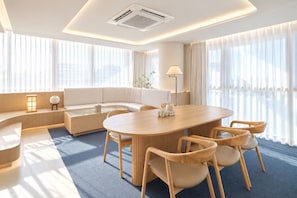 A modern hotel room with a round dining table, comfortable seating, a sofa, and large windows with sheer curtains. - UH Suite The Gangnam (Seoul)