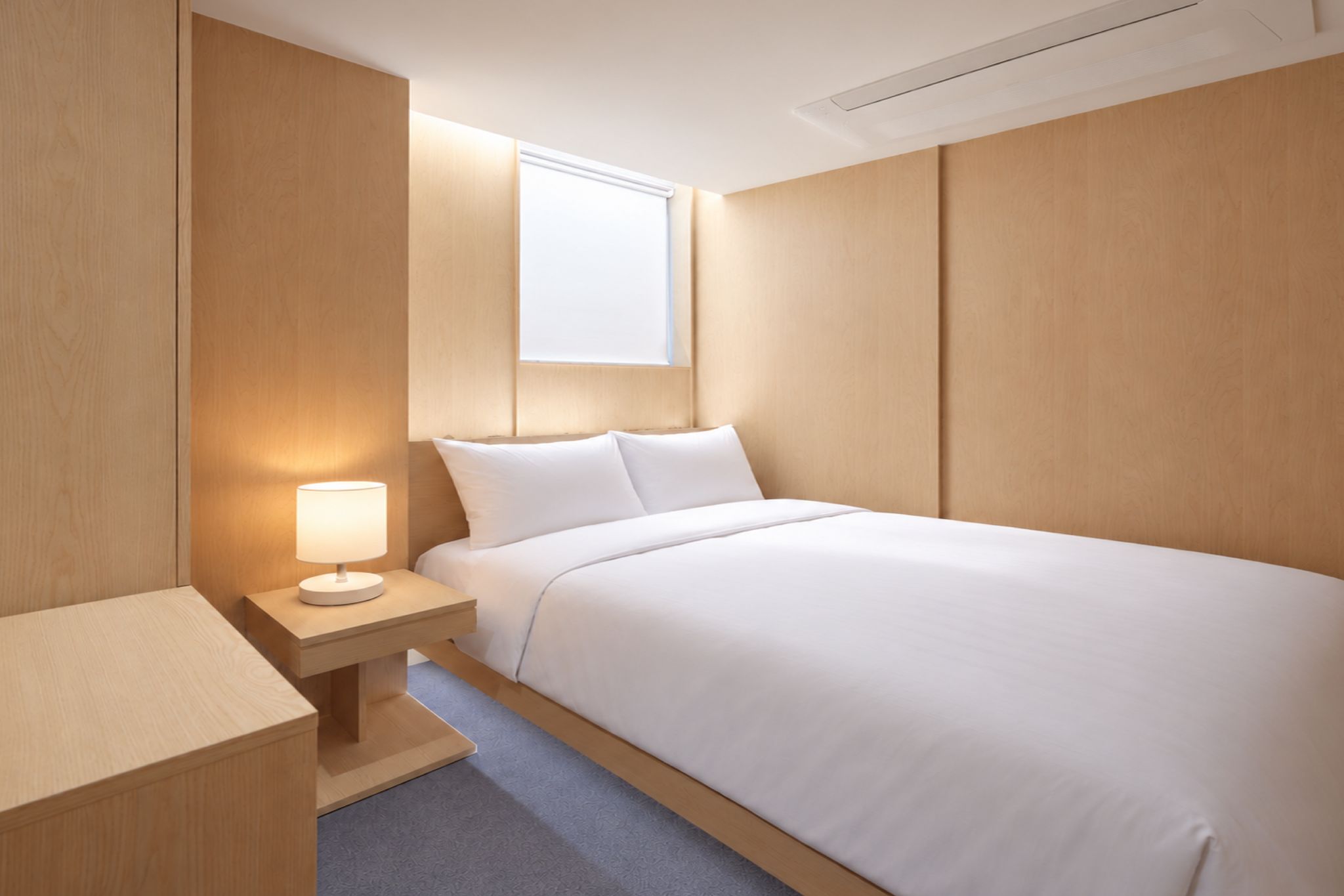 Una habitación de hotel con una cama, una mesita de noche con lámpara y una ventana.