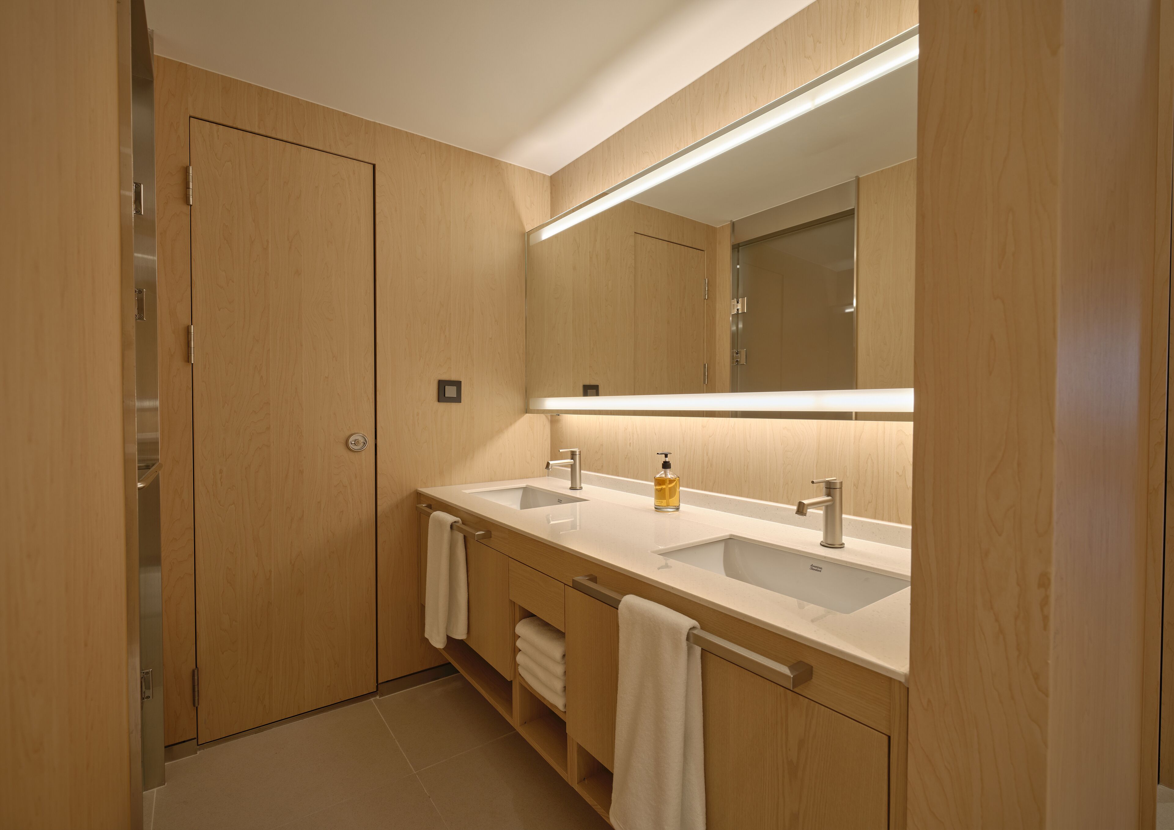 A modern bathroom with wooden cabinetry, two sinks, a large mirror, and a towel rack.