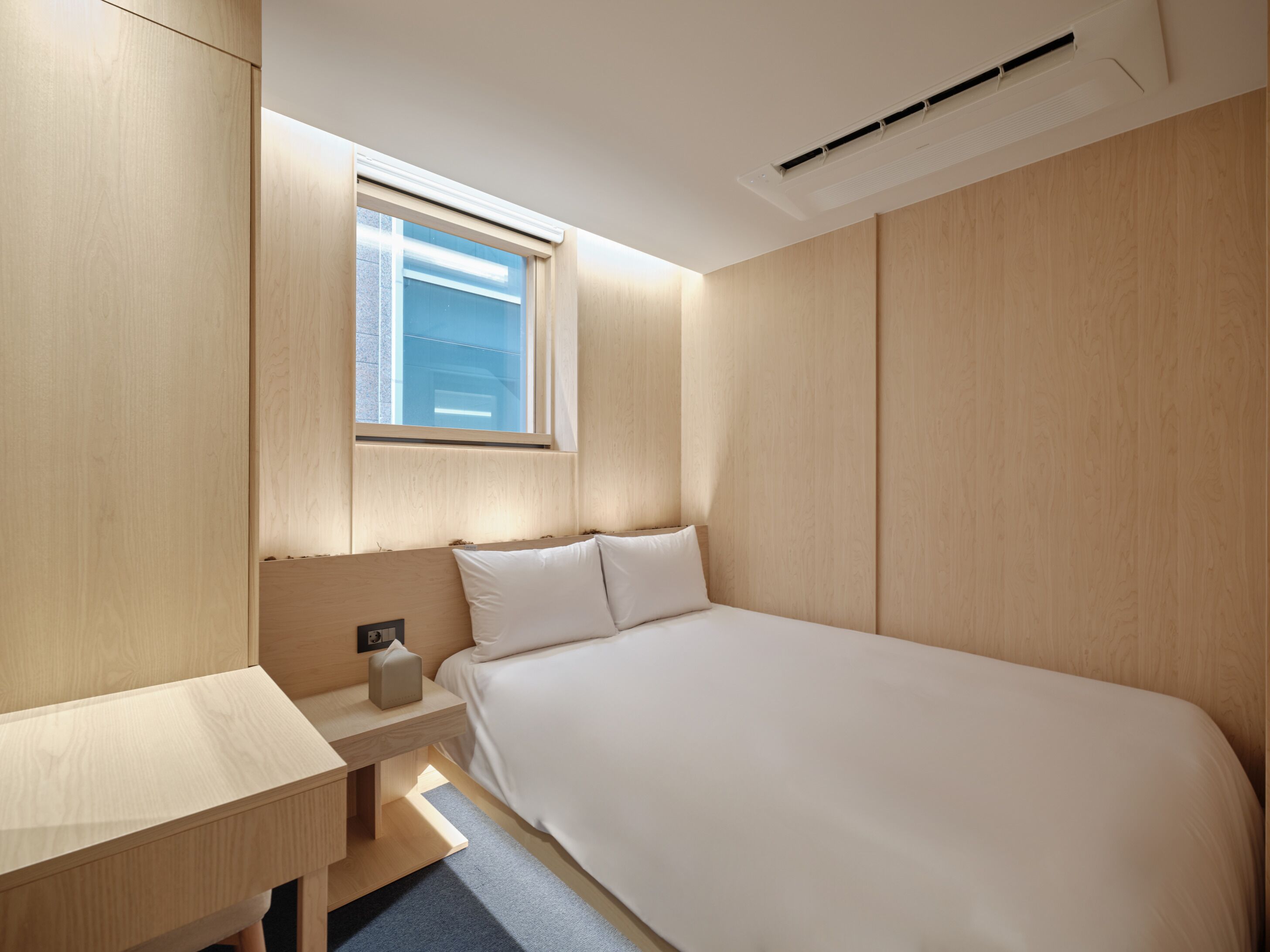 A modern bedroom with a wooden headboard, a bedside table with a lamp, and a large bed.