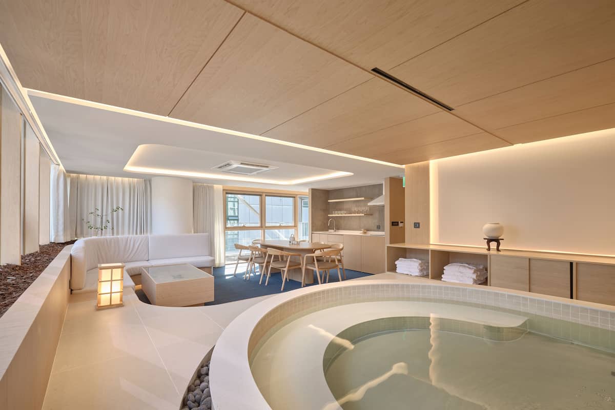 Habitación de hotel moderna con un jacuzzi curvo, un comedor y una zona de estar con sofá y una mesita.
