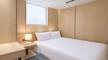 A hotel room with a bed, bedside table, lamp, and a window.