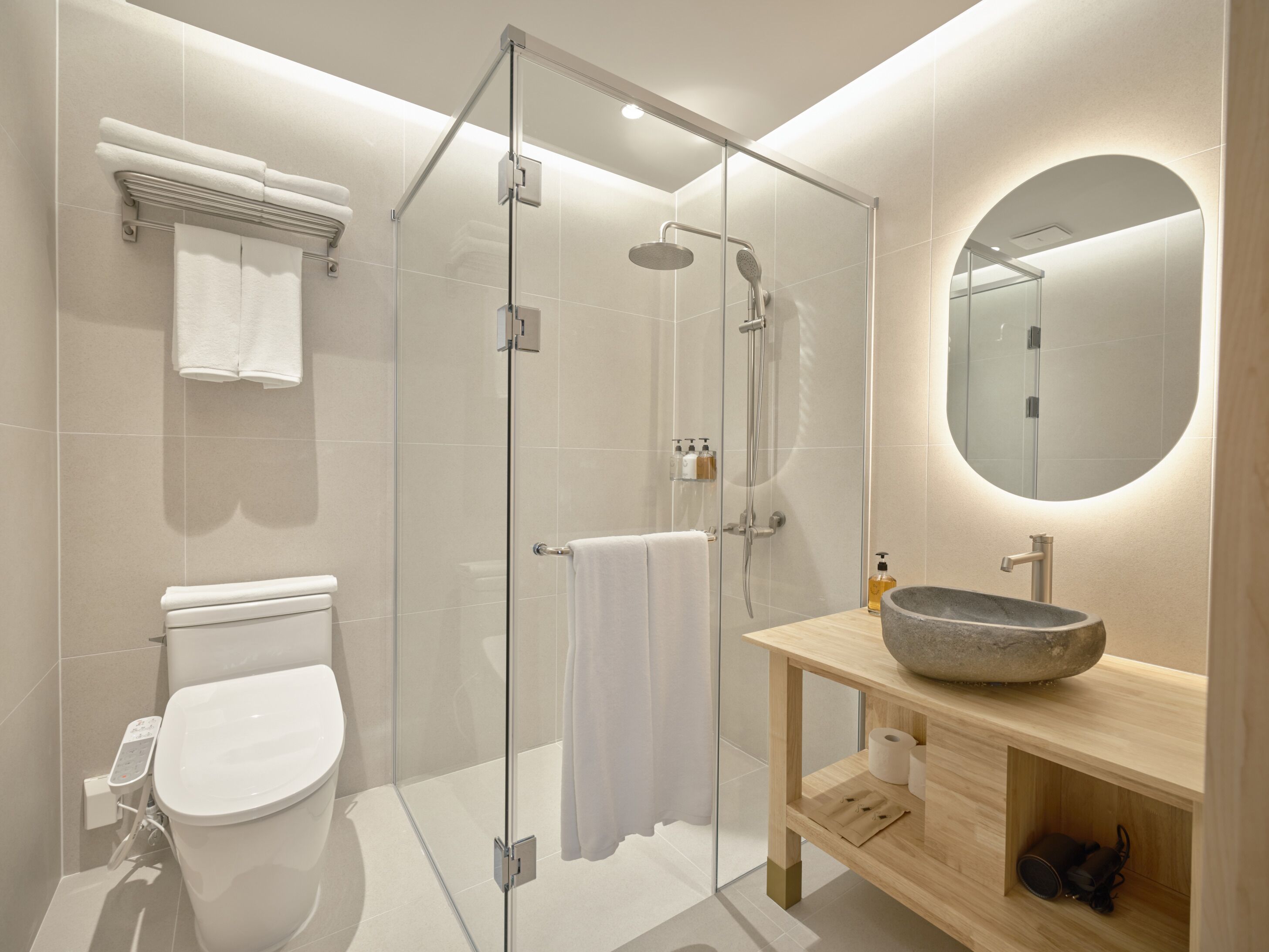 A modern bathroom with a glass-enclosed shower, a toilet, a sink with a stone basin, and a mirror with a circular frame.