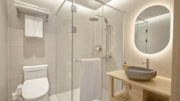A modern bathroom with a glass-enclosed shower, a toilet, a sink with a stone basin, and a mirror with a circular frame.