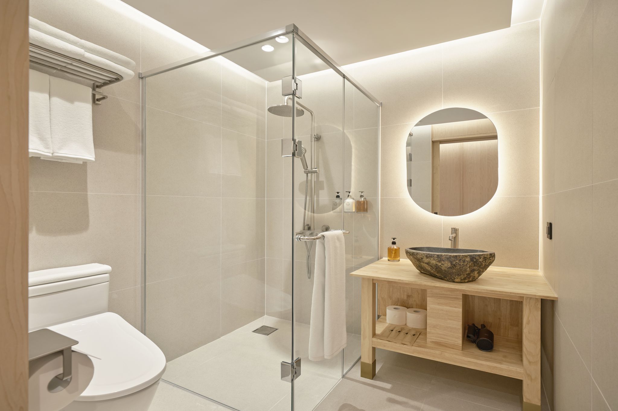 Un baño moderno con ducha acristalada, un espejo redondo y un tocador de madera con lavabo.