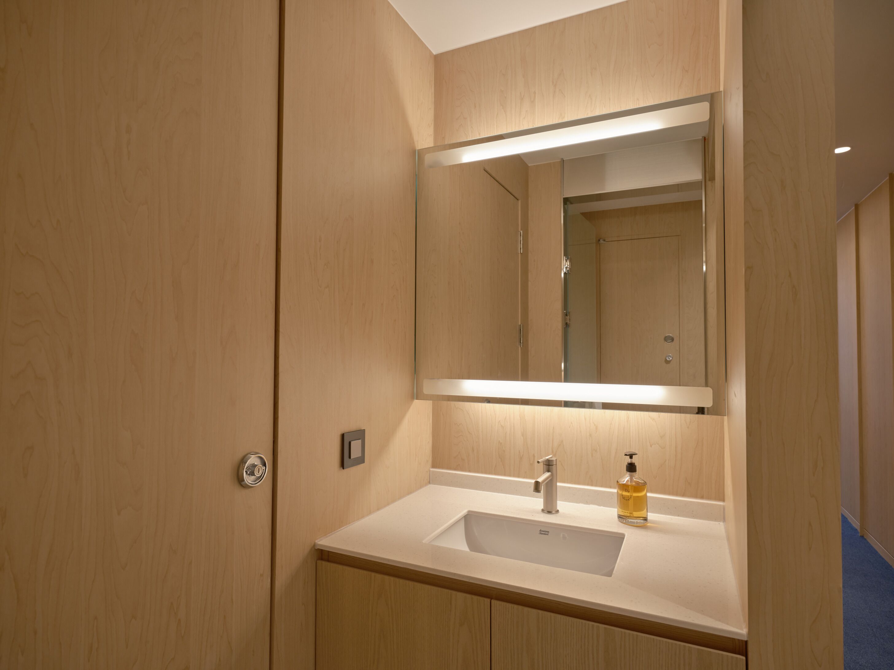 A hotel bathroom with a wooden vanity, a sink, a mirror, and a bottle of hand soap.