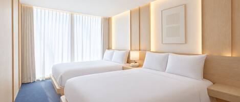 Habitación de hotel con dos camas, un ventanal con cortinas, una mesita de noche con lámpara y un cuadro en la pared.