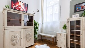 A room with a large white cabinet, a small bench, and a television displaying a fire.