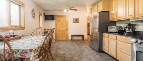 Una cocina con armarios de madera, un refrigerador, un microondas y una mesa de comedor con sillas.