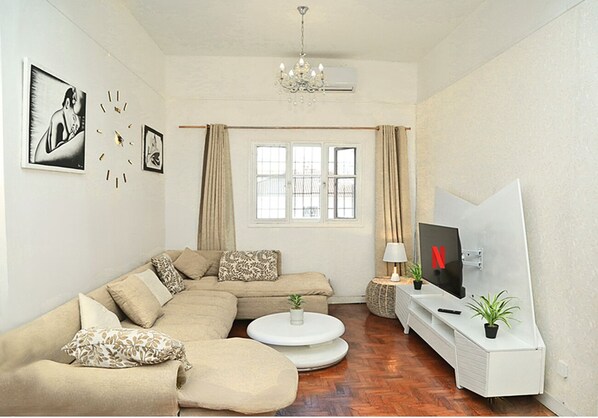 A living room with a sectional sofa, a coffee table, a TV, and a chandelier.